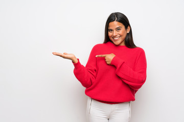 Young Colombian girl with red sweater holding copyspace imaginary on the palm to insert an ad