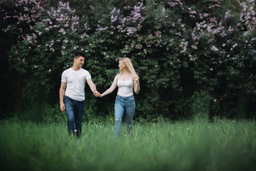 Fototapeta premium A young couple in love holding hands and walking forward in front of a flowering bush