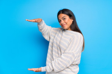Young Colombian girl with sweater holding copyspace to insert an ad