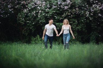 A young couple in love holding hands and walking forward in front of a flowering bush