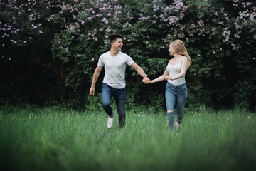 Naklejka na ściany i meble A young couple in love holding hands and running forward in front of a flowering bush