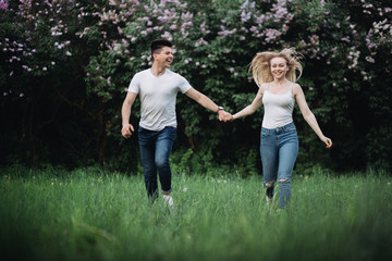 Obraz premium A young couple in love holding hands and running forward in front of a flowering bush