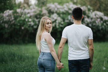 A young couple in love holding hands and walking towards the flowering bush