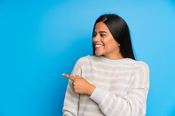 Young Colombian girl with sweater pointing finger to the side