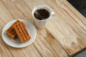 Hot coffee on a wooden stand with waffle, top view