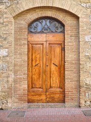 Fototapeta na wymiar A wood door with an orange wrought iron window set in a arched doorway of a brown brick building in Tuscany Italy