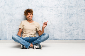 Young african american man sitting on the floor pointing finger to the side