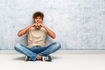 Young african american man sitting on the floor showing a sign of silence gesture