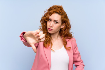 Redhead woman in suit over isolated blue wall showing thumb down with negative expression