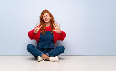 Redhead woman with overalls sitting on the floor counting eight with fingers