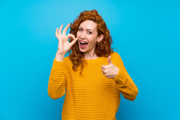 Redhead woman with yellow sweater showing ok sign and thumb up gesture