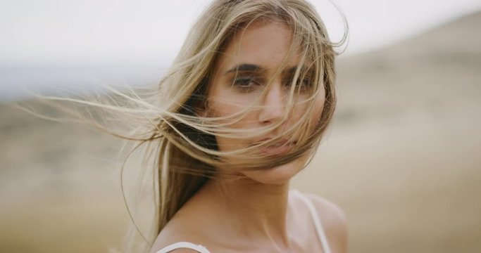 Portrait of beautiful young woman looking into the camera with her hair blowing in the wind in slow motion, bohemian bride lifestyle