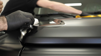Two professional masters in car painting and ceramics overlay a layer of ceramics using a micro fiber and cloth, in a car deteyling center. Concept of: Service, New car, Refresh.