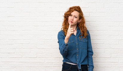 Redhead woman over white brick wall frustrated and pointing to the front