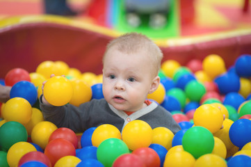 The boy sits in a pile of balls in a dry pool and plays