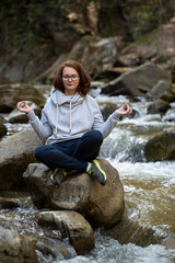 Young woman doing yoga zen on a rock in the middle of the river in a forest