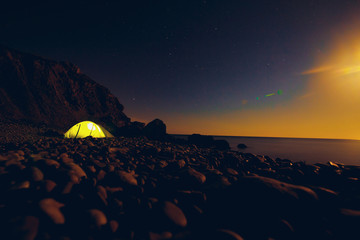 Light in a tent by the sea on the rocks in the starry night
