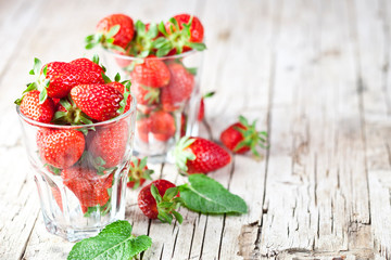 Organic red strawberries in glass and mint leaves on rustic wooden background. Healthy sweet food, vitamins and fruity concept.