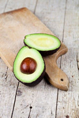 Fresh organic avocado halves on cutting board on old wooden table background.