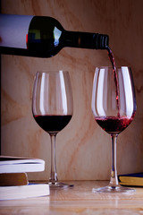 Pouring red wine into the glass against wooden background