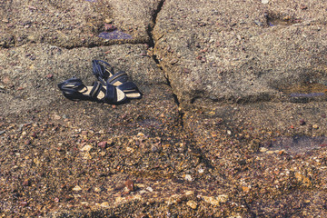 empty old female sandals on stone coast background 