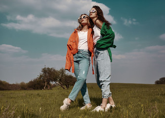 High fashion portrait of two stylish beautiful woman in trendy jackets and jeans posing outdoor....