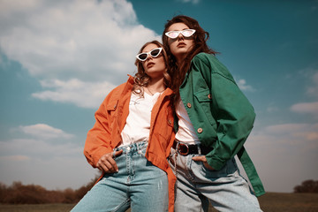 High fashion portrait of two stylish beautiful woman in trendy jackets and jeans posing outdoor....