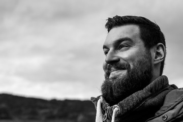 Young attractive bearded man with dark hair and a pullover in the park smiling