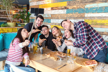 Best friends taking selfie with funny faces while sharing pizza at restaurant