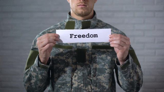 Freedom word written on sign in hands of male soldier, peace, end of war
