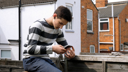 teen boy with smart phone listening or talking while sitting in british backyard garden. teenager and social media concept