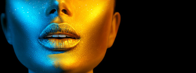 Fashion model woman face in bright sparkles, colorful neon lights, beautiful sexy girl lips. Trendy glowing gold skin make-up. Wide screen