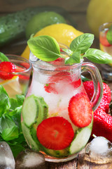 Cucumber strawberry basil lemonade with ice in jug, vintage wooden table, selective focus