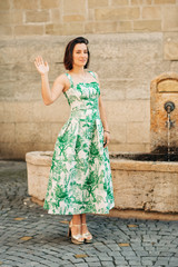 Outdoor fashion portrait of beautiful woman with dark hair, wearing long vintage styled green dress, posing on the city street