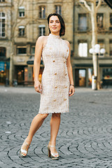 Outdoor fashion portrait of beautiful woman with dark hair, wearing fashionable dress, posing on the city street