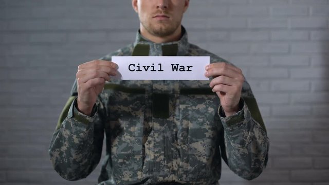 Civil war word written on sign in hands of male soldier, cruelty and death