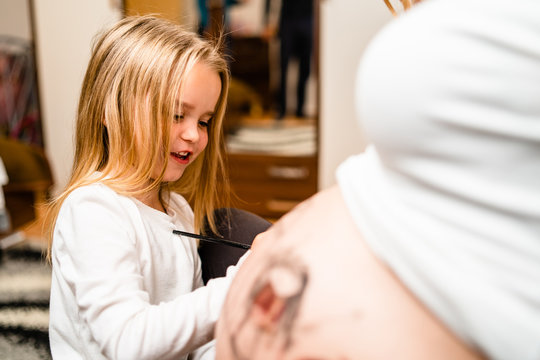 Little blonde girl painting little baby brother or sister on her mothers pregnant belly with water colors