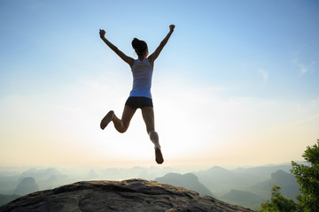 Fototapeta na wymiar Successful freedom woman jumping on sunrise mountain top
