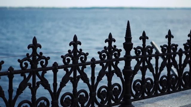 Black metal fence on the background of water. Decorative fence in the form of a balustrade. The camera moves along the fence. Close up