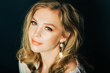 Close up portrait of beautiful young woman with blond hair and professional make up, posing on black background