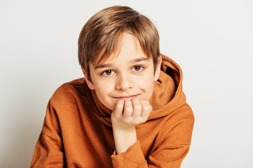 Studio shot of handsome 10 year old boy with blond hair, wearing brown hoody, posing on white...