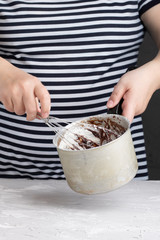 professional cook mixes dough, chocolate cream and eggs by whisk for dessert