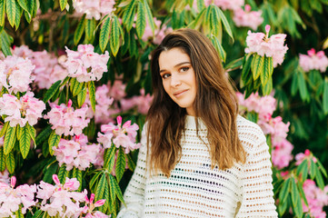 Outdoor portrait of beautiful young woman white knitted pullover, posing in spring garden