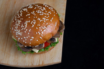 big homemade burger with fried mushrooms, cheese and tomato slice, crispy bun with sesame