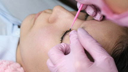Obraz na płótnie Canvas Eyelash extension procedure. Female eyes with long eyelashes. Cosmetic procedure in spa salon. Beautician tints false eyelashes