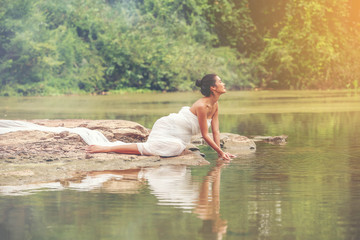 Beautiful sexy women in white light dress sitting on the rock. Sexy model sitting along the lake quiet and peace place for relaxation.
