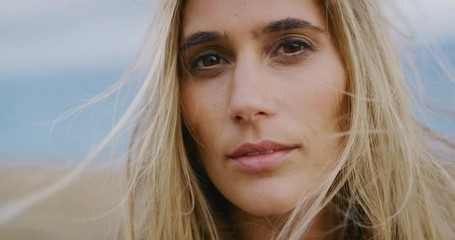 Close up portrait of beautiful golden young woman turning and looking into the camera with kind eyes and her hair blowing in the wind - Powered by Adobe
