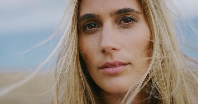 Close up portrait of beautiful golden young woman turning and looking into the camera with kind eyes and her hair blowing in the wind