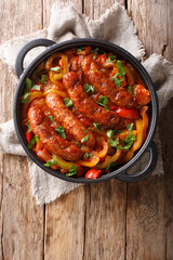Italian food grilled sausage with grilled peppers, onions, herbs and tomatoes closeup in a frying pan. Vertical top view