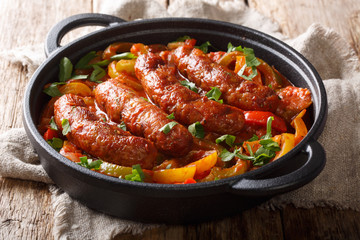 Grilled homemade sausages with colored peppers, onions, herbs and tomatoes closeup in a frying pan. horizontal
